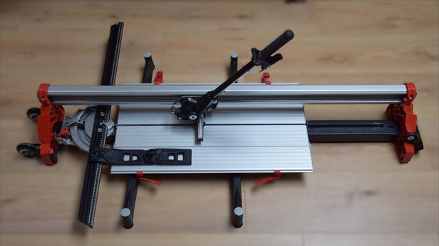Overzicht van tegelsnijder op houten vloer met aluminium geleiding en rode accenten