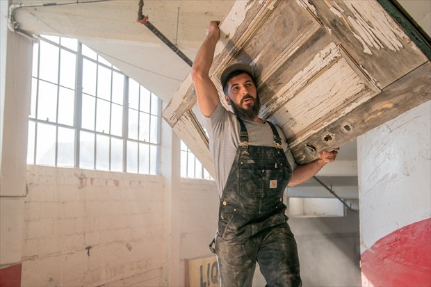 Man draagt oude houten deur op schouder terwijl hij een Carhartt BIB overall draagt