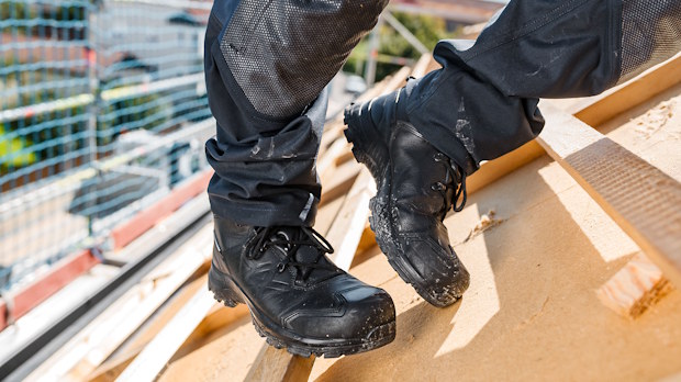 Close-up of black work boots stepping on wooden roof framing at a construction site.
