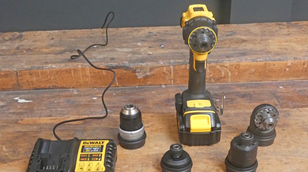Cordless yellow-and-black drill with battery on a wooden workbench, surrounded by drill bits and a charger pad.