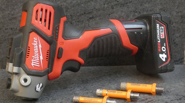 Milwaukee cordless power tool with a large battery on a dark surface, orange/black body and attachments nearby.