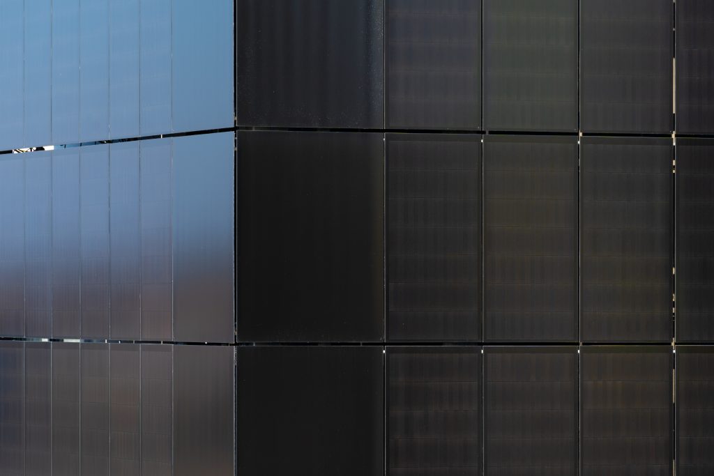 Close-up of a building facade showing blue vertical panels on the left and dark panels on the right with visible seams.