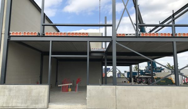 Construction site with a steel-framed building under construction; interior shows a red chair and table at ground level.